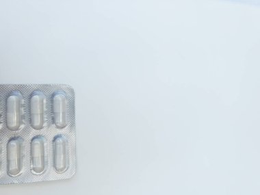 Detaylı bir makro çekimde birkaç kapsülü olan bir su toplayıcı sergileniyor. Paket pürüzsüz beyaz bir yüzeye yerleştiriliyor, ilaç tasarımı ve rengine odaklanmayı arttırıyor.