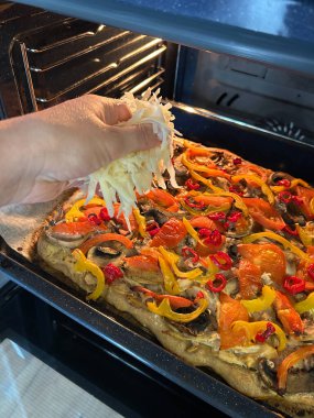 Fırındaki yeni pişmiş pizzaya renkli sebze ve peynir dilimleri ekleniyor. Sıcak ortam, ev yapımı yemekler için mükemmel, rahat bir yemek atmosferi sağlıyor..