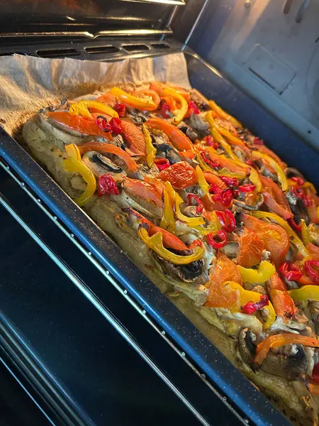 Dilimlenmiş dolmalık biber, mantar ve doğranmış domatesle kaplı bir fırında ekmek pişiriliyor. Canlı renkler iştah açıcı bir görsel yaratıyor, sağlıklı bir yemek için mükemmel..