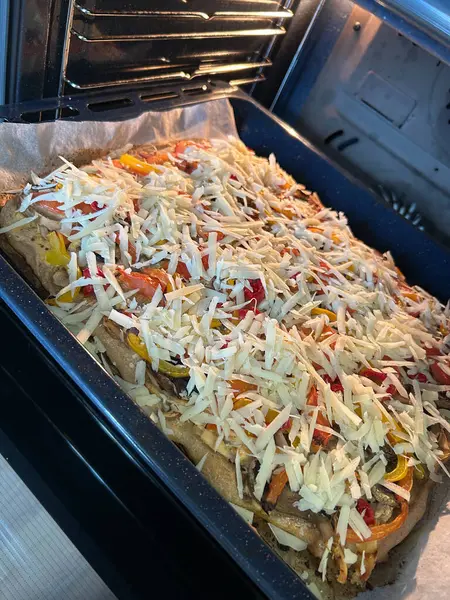 Sebze ve peynirle dolu taze pişmiş bir tabak fırının içindeki bir fırın tepsisinde oturur. Malzemelerin canlı renkleri erimiş peynirle tezat oluşturuyor. Bu da lezzetli bir yemeğin hazırlandığını gösteriyor..