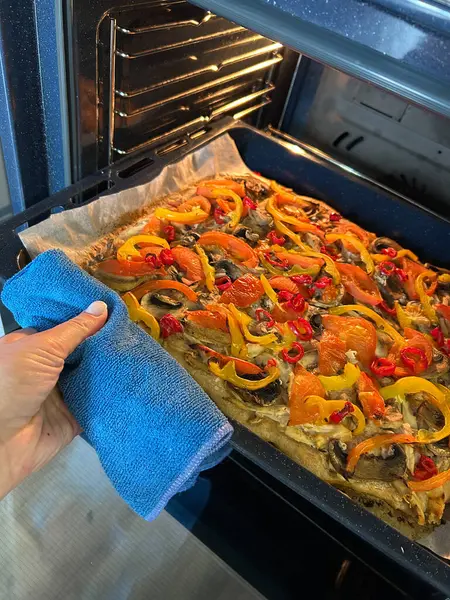 Parlak renkli sebzeler fırında pişiyor, biber, mantar ve vişneli domates karışımı sergiliyorlar. Bir el mutfak havlusunu tutar, tepsiyi çekmeye hazır..