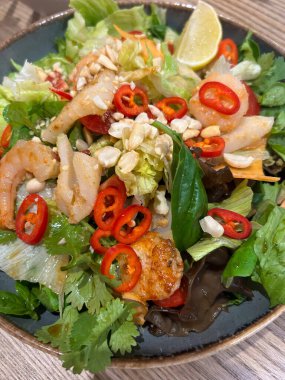 İçinde karides, taze yeşiller, otlar ve kırmızı biber dilimleri olan canlı bir salata. Çıtır çıtır sebzeler ve ezilmiş fıstıklar lezzet dokunuşu için limon dilimli doku ekler..