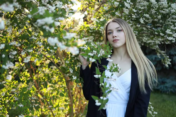 Genç bir kadın çiçek açan bitkilerle çevrili verimli bir bahçede zarif bir şekilde duruyor. Sıcak güneş ışığı huzurlu bir atmosfer yaratıyor, sakin ifadesini arttırıyor..