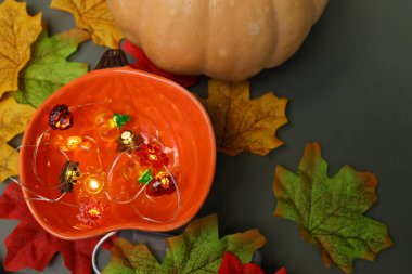 Parlak sonbahar süslemelerinde renkli yapraklar ve balkabağının arasına yerleştirilmiş ışıklarla dolu canlı bir turuncu kâse bulunur. Sonbahar sezonunun özünü yakalar..