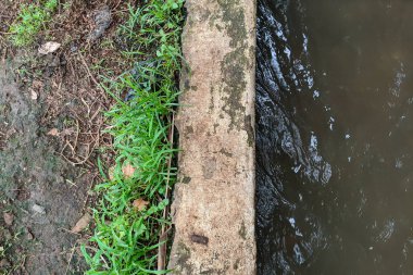 Küçük bir su yolu, muhtemelen bir hendek ya da kanal, aşınmış beton bariyerlerle çevrili..