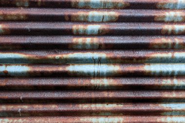 Yoğun paslanmış, kahverengi, pas ve gri tonlarıyla kıvrımlı metal bir levhanın yakın görüntüsü..