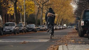 Berlin, Almanya - 10 Kasım 2021: Güzel bir sonbahar gününde Bergmannstrasse 'de bir mezarlığın yanında altın sarısı yapraklarla bisiklet süren bisikletçi. Atanmış bisiklet sokağı.