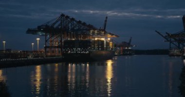 HAMBURG, 2013: Büyük Gantry Turnaları (Konteyner Turnaları) ile birlikte Hamburg limanında Magic Hour (alacakaranlık) sırasında bir Kargo Gemisi / Kargo gemisinden boşaltılan konteynırlar. Kırmızı 'da çekim.