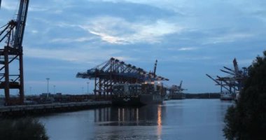 Güneş Hamburg limanında büyük Gantry Turnaları (Konteyner Turnaları) ile batarken konteynırların bir konteynır gemisi / kargo gemisinden indiriliş zamanı.