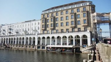 HAMBURG, ALMANY - 27 Mart 2022: Alsterarkaden boyunca Pan, Alster Çarşısı, nehir kıyısında bir alışveriş merkezi, güneşli bir bahar günü mavi gökyüzü ile Canal Alster. Restoranlar ve kafelerle..