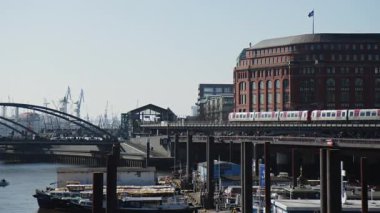 HAMBURG, ALMANY - 27 Mart 2022: Hochbahn, Metro Treni, Subway, arka planda Hamburg Limanı ile Baumwall İstasyonu 'na doğru hareket ediyor. Konteynır Turnaları güneşli bir günde gökyüzüne karşı siluetlendi