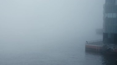 2022 'de Hamburg Limanı' ndaki Groe Elbstrae, Holzhafen 'daki iskelede yoğun sisi araştıran yalnız bir insan. Gizemli, atmosferik ve ürkütücü görünüyor. Yoğun Sisweather condition.