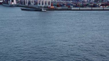 HAMBURG, GERMANY - 19 Mart 2022 'de Elbe Nehri' nin suyundan alacakaranlıkta Hamburg Limanı 'nda yüklenen konteyner gemilerine doğru eğilin. Konteynır besleme gemisi geçiyor. Taşınmış konteynırlar