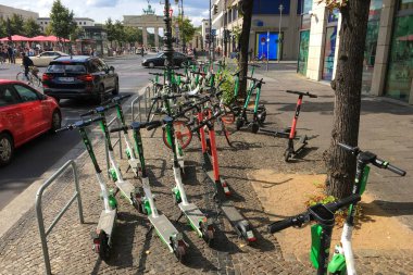 BERLIN - SEPTEMBER 08, 2019: Many Electric E-Scooters of different Ride Sharing Companies parked chaotically on a sidewalk in Berlin close to the Brandenburg Gate. Modern and trendy City Transport clipart