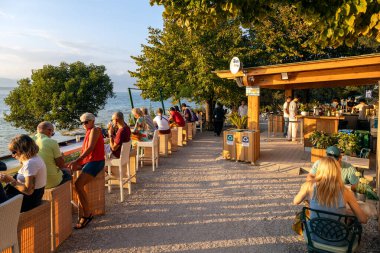 Sirmione, İtalya - 21 Eylül 2024: İnsanlar Garda Gölü 'ne bakan göl kenarındaki bir barda rahat bir günbatımının keyfini çıkarıyorlar