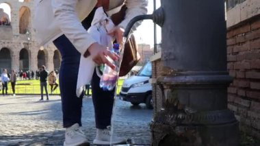 Roma, İtalya - 15 Kasım 2024: Bir kişi Nasone 'da bir şişe dolduruyor, arka planda Colosseum olan ücretsiz bir çeşme. 