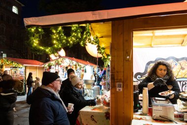 Lugano, İsviçre - 23 Aralık 2024: Bir Noel pazarında ziyaretçiler gece dekorasyon ve ışıklarla ziyafet çekiyorlar