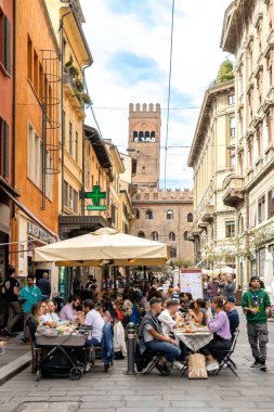 Bologna, İtalya - 15 Eylül 2024: Açık havada yemek yiyen insanlarla dolu bir cadde ve arka planda Torre dellArengo