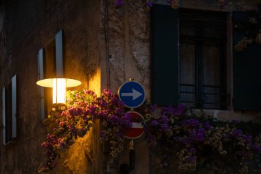 A glowing streetlight highlights bougainvillea and traffic signs in Sirmiones historic center at night, Italy clipart