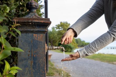 İtalya 'nın Sirmione kentindeki geleneksel bir Nasone çeşmesinde el yıkayan kişi, arkada Garda Gölü var.
