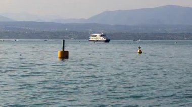Garda Gölü 'nün sularında bir feribot, yakınlarda tekneler ve arkada dağlar, Sirmione, İtalya' da.