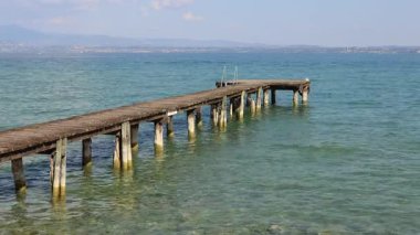 Sirmione, İtalya 'da güneşli bir günde Garda Gölü' nün berrak sularına uzanan ahşap iskele.