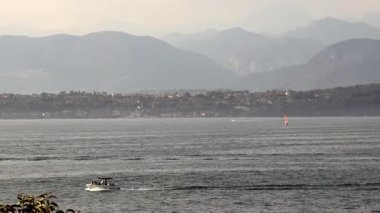 Sirmione, İtalya - 21 Eylül 2024: Turistler Garda Gölü 'nde tekne gezintisi yapıyorlar, jet ski ve yelkenliyle manzaralı bir dağ zeminine doğru ilerliyorlar