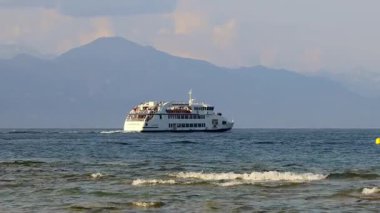 Sirmione, İtalya - 21 Eylül 2024: Arka planda dağlarla Garda Gölü 'nü geçen bir feribot