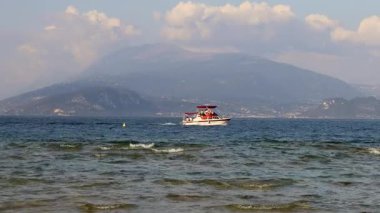 Sirmione, İtalya - 21 Eylül 2024: Garda Gölü 'nde tur teknesi ve jet ski, arka planda dağlar