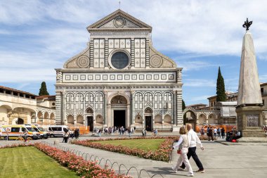 Florence, Italy - May 11th, 2025: Visitors walk past the Basilica of Santa Maria Novella and blooming gardens in the historic square