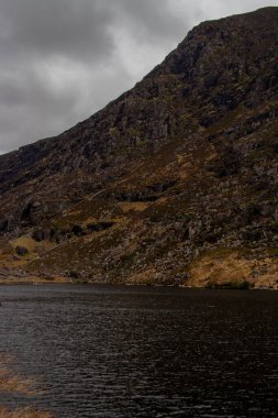 Killarney, İrlanda 'daki Killarney Ulusal Parkı' ndaki Dunloe Geçidi 'nden geçen yol engebeli dağlar ve yuvarlanan yeşil tepeler arasında zarif bir şekilde kıvrılarak bir kurdele gibi uzanıyor. Sahne yüksek bir görüntü yakalar