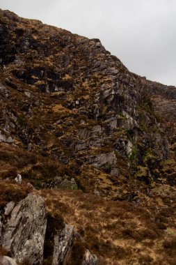 Dağıtılmış taşlar, zamanla pürüzsüz yıpranmış, yeri noktalıyor, sarp kayalıklarla kusursuz bir şekilde harmanlanıyor, her iki tarafta keskin bir şekilde yükselen dağların taş ferahlığı. Uçurumlar derin yarıklarla dolu.