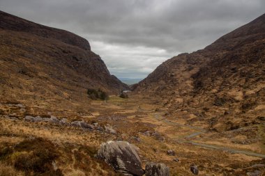 Killarney, İrlanda 'daki Killarney Ulusal Parkı' ndaki Dunloe Geçidi 'nden geçen yol engebeli dağlar ve yuvarlanan yeşil tepeler arasında zarif bir şekilde kıvrılarak bir kurdele gibi uzanıyor. Sahne yüksek bir görüntü yakalar