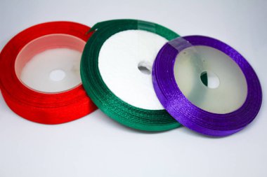 Beyaz arkaplanda çeşitli kırmızı, yeşil, mor saten kurdeleler var.