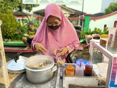 Endonezya, Solo - 11 Aralık 2024: Asyalı kadın müşteri için pentol siparişi hazırlıyor