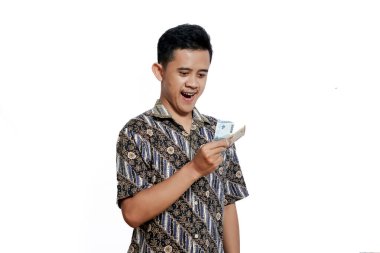 Batik tişört giyen Asyalı bir adam beyaz arka planda izole edilmiş mutlu bir ifadeyle elinde biraz para tutuyor.