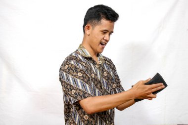 Parang desenli batik kıyafetler giyen Asyalı adam boş cüzdana bakıyor.