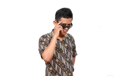 Asyalı erkek manken portresi batik gömlek ve güneş gözlüğü takıyor ve gülümsüyor, beyaz arka planda izole edilmiş.