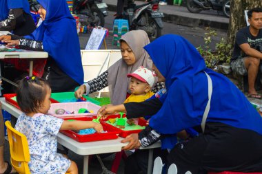 Indonesia, Solo - December 22, 2024: a group of children playing a game of making cake replicas accompanied by their mothers. clipart