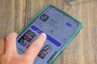 Endonezya, Solo - 26 Aralık 2024: Ahşap masada izole edilmiş cep telefonu üzerinde çalışan TikTok uygulama simgesine parmak dokunuşu