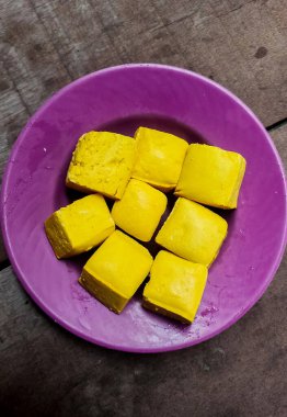Ahşap masa arkasına izole edilmiş mor plastik tabakta çiğ tofu.