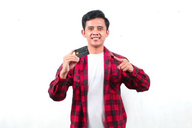 Kareli gömlek giyen Asyalı adam, beyaz arka planda izole edilmiş, neşeli yüzüyle kredi kartı gösteriyor.