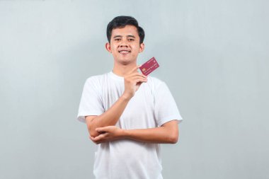 Beyaz t-shirt giyen Asyalı adamın kredi kartı gri arka planda. İş, finans, ekonomi konsepti