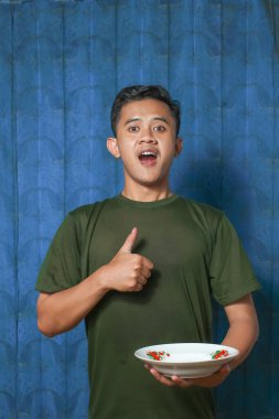 Asyalı adam boş tabağı tutarken mavi perde arkaplanına başparmak işareti yapıyor