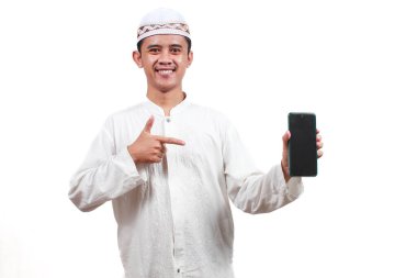 Asyalı Müslüman adam mutlu bir şekilde beyaz arkaplan ve dini kavramlarla boş cep telefonu ekranına parmağını gösteriyor.