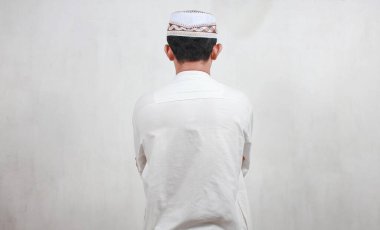 Beyaz bir duvarda dua eden Asyalı Müslüman bir adamın portresi.