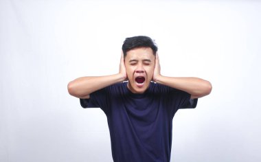 Asyalı adam iki kulağını da iki eliyle sıkıca kapatıyor. Beyaz arka planda izole edilmiş kızgın bir ifade sergiliyor.