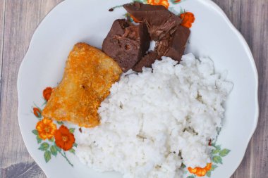 Kahvaltı menüsü, gudeg sebzesi ve mayonez dolu sosis masada cam tabakta servis ediliyor.