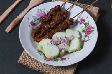 Endonezya spesiyalitesi tavuk satay ve dilimlenmiş çiğ soğan serpiştirilmiş seramik tabakta. Siyah bir arkaplanda izole edilmiş