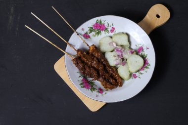 Endonezya spesiyalitesi tavuk satay ve dilimlenmiş çiğ soğan serpiştirilmiş seramik tabakta. Siyah bir arkaplanda izole edilmiş